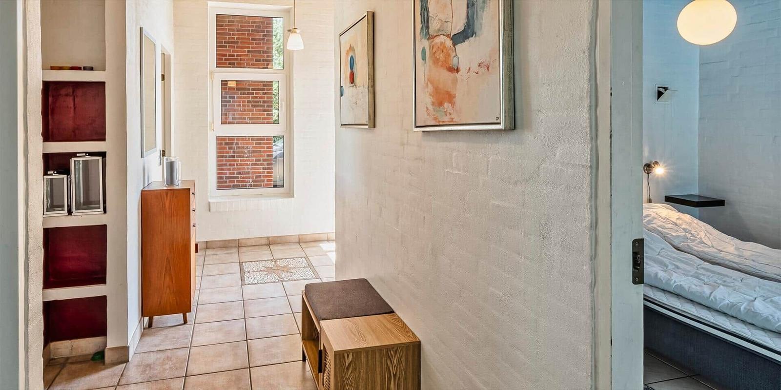 Hallway with wooden bench, wall art, and view into bedroom with bed.