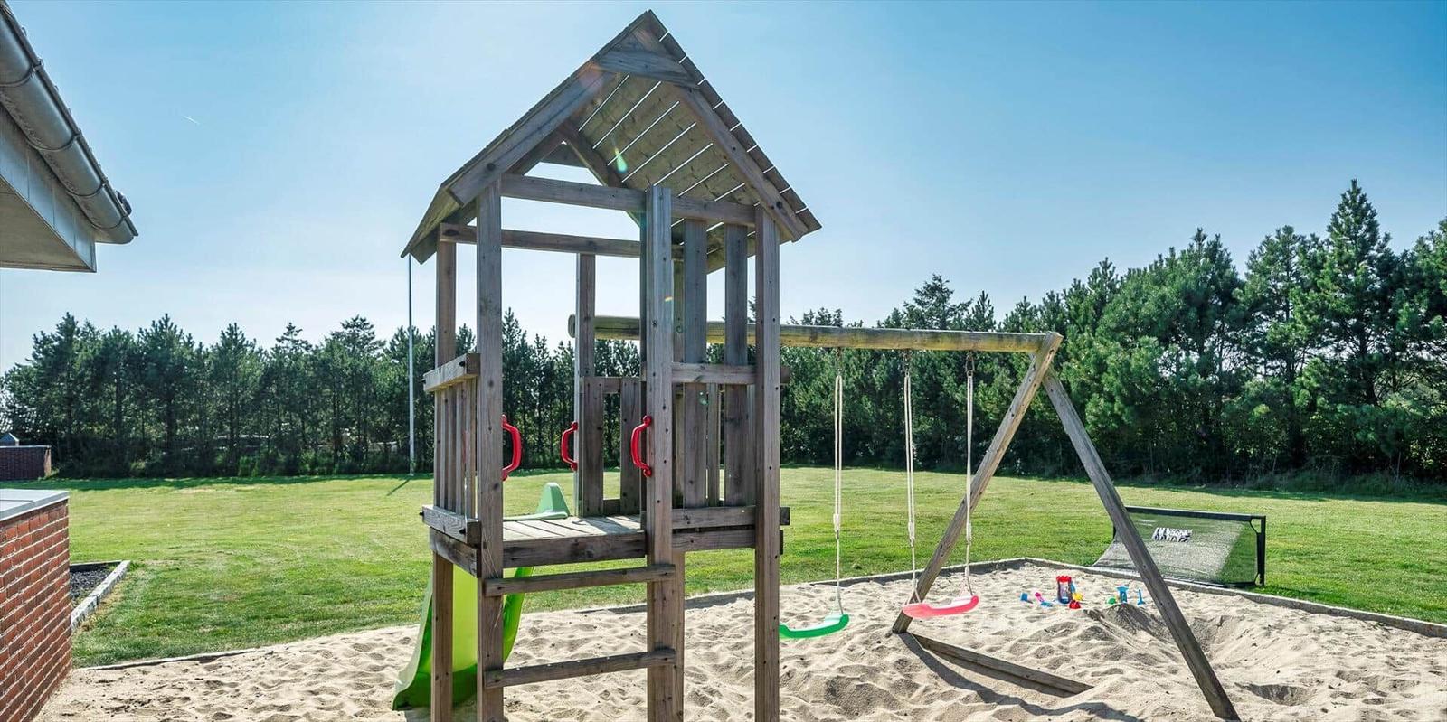 Wooden playground with slide, swings, and sandbox on green lawn.