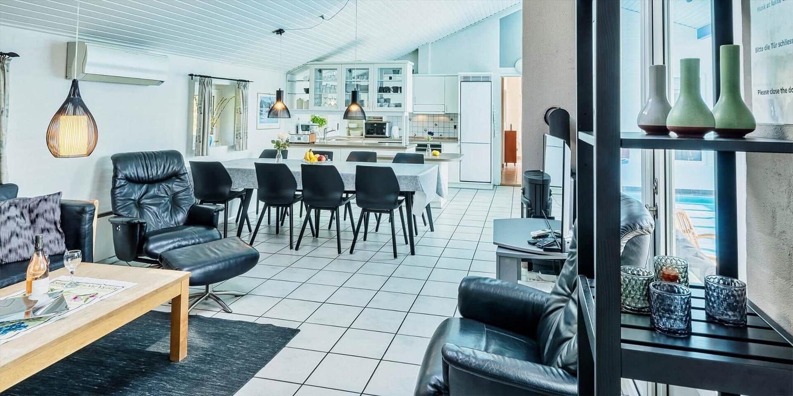 Living and dining area with kitchen, black leather chairs, and white tiled floor.