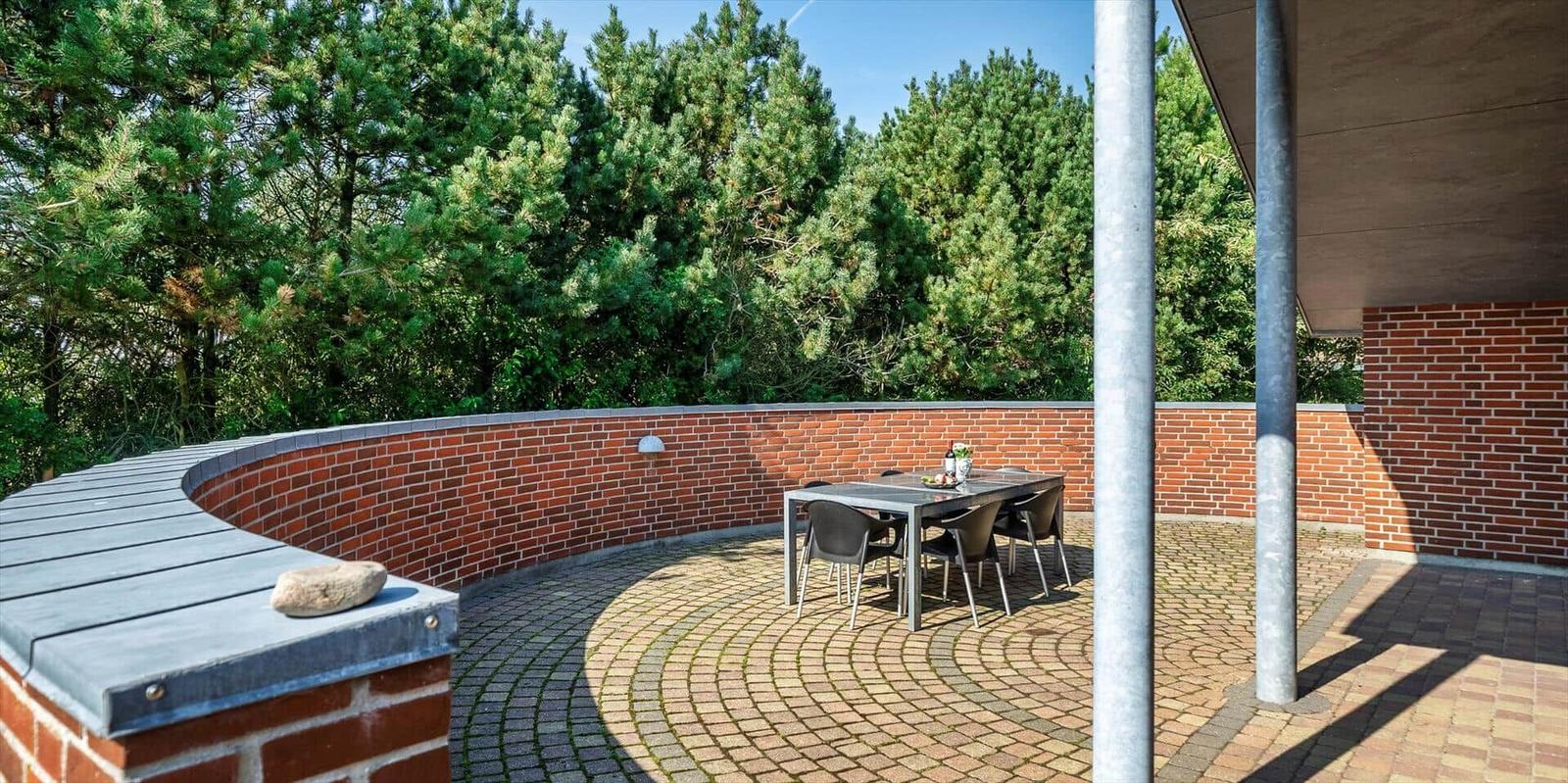 Terrace with table and chairs, surrounded by red bricks and trees.