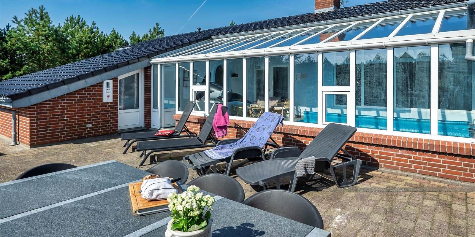 Terrace with sun loungers and view into the glass conservatory with pool.