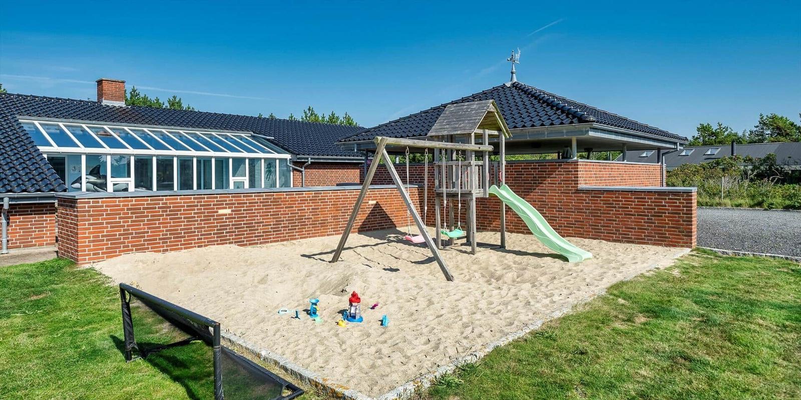 Behind the house is a sandbox with play equipment and a green slide.