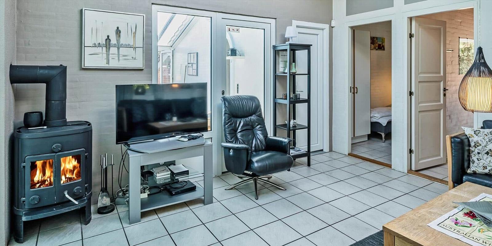 Living room with fireplace, TV, and leather armchair. Door leads to bedroom.