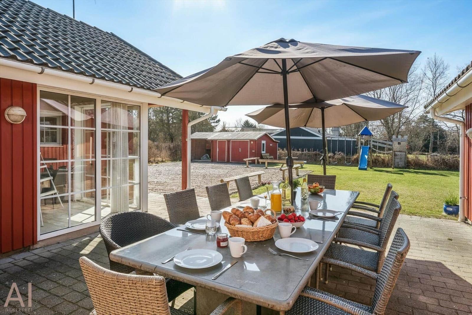 Terrace with table, chairs, and umbrella. Playground and garden in the background.