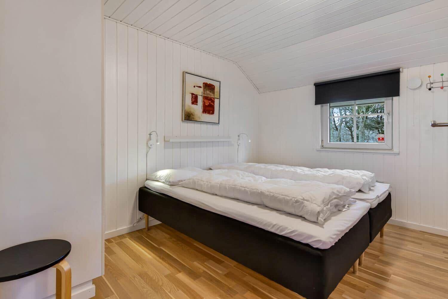 Bedroom with double bed, wooden floor, and window with view of trees.