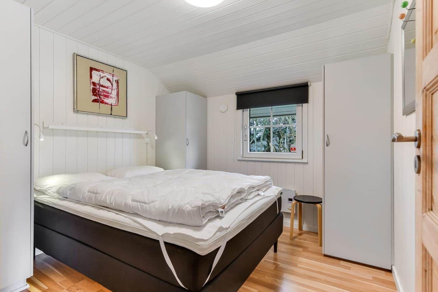 Bedroom with bed, window, and closets. Wooden floor and white walls.