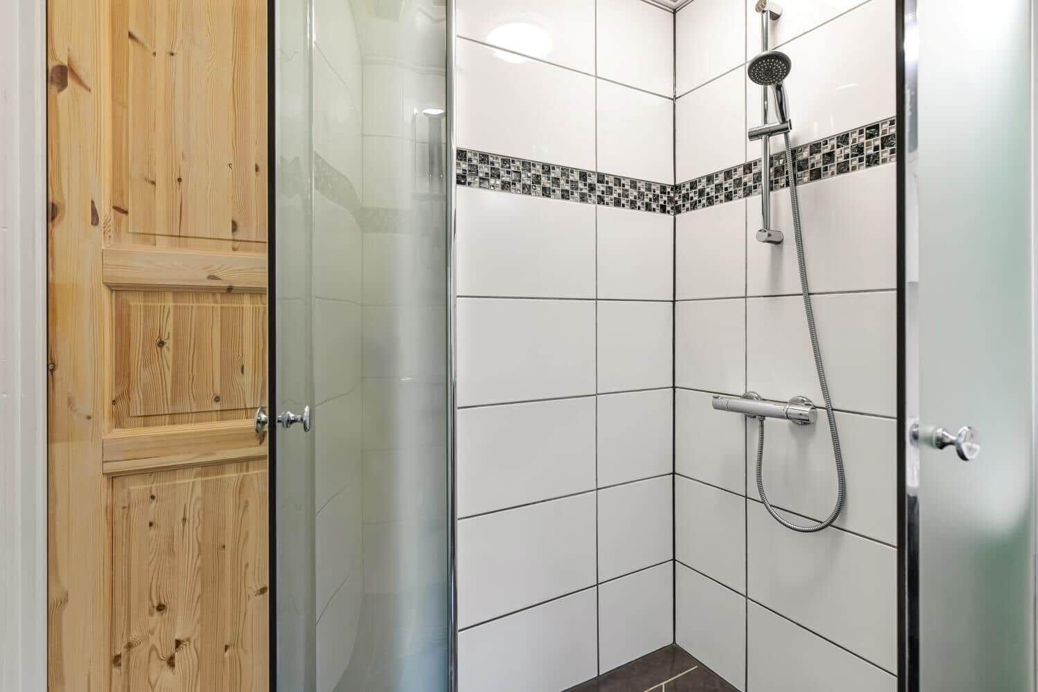 Shower cabin with glass door and showerhead, wall tiles with mosaic strip.