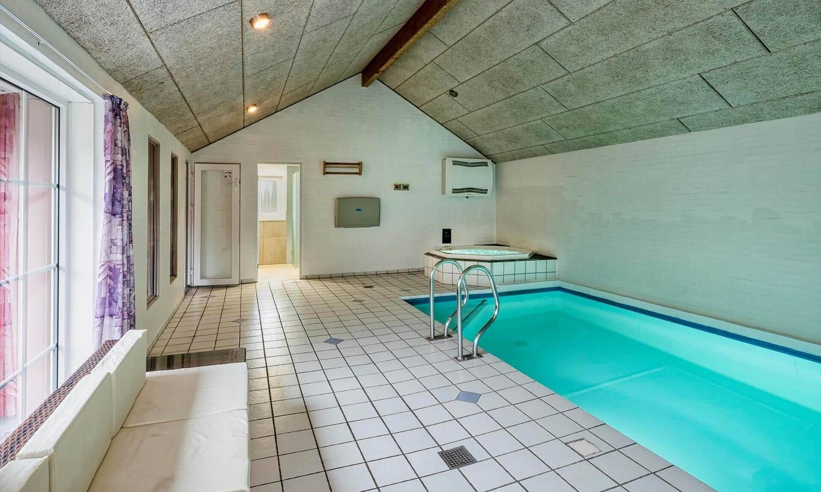 Indoor pool and hot tub with window and bench.