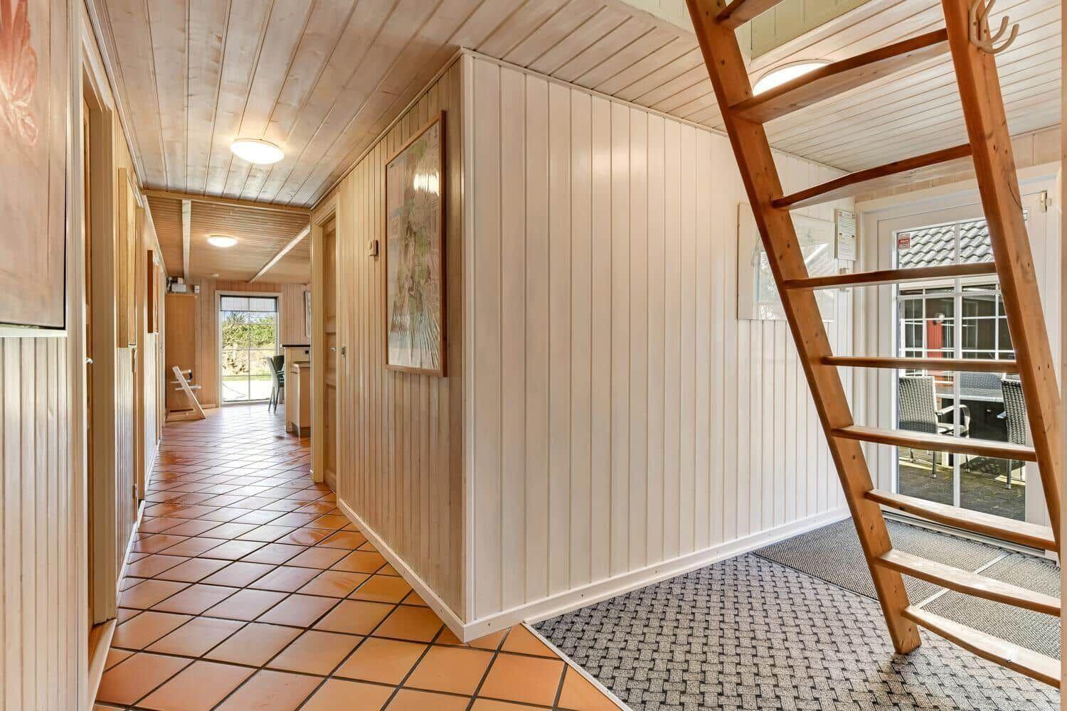 Hallway with wooden wall and ladder to upper level. Terrace with garden furniture visible.