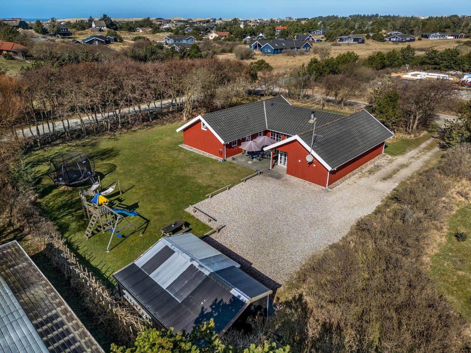 Red vacation house with garden, playground, and barbecue area. View of coastal landscape.