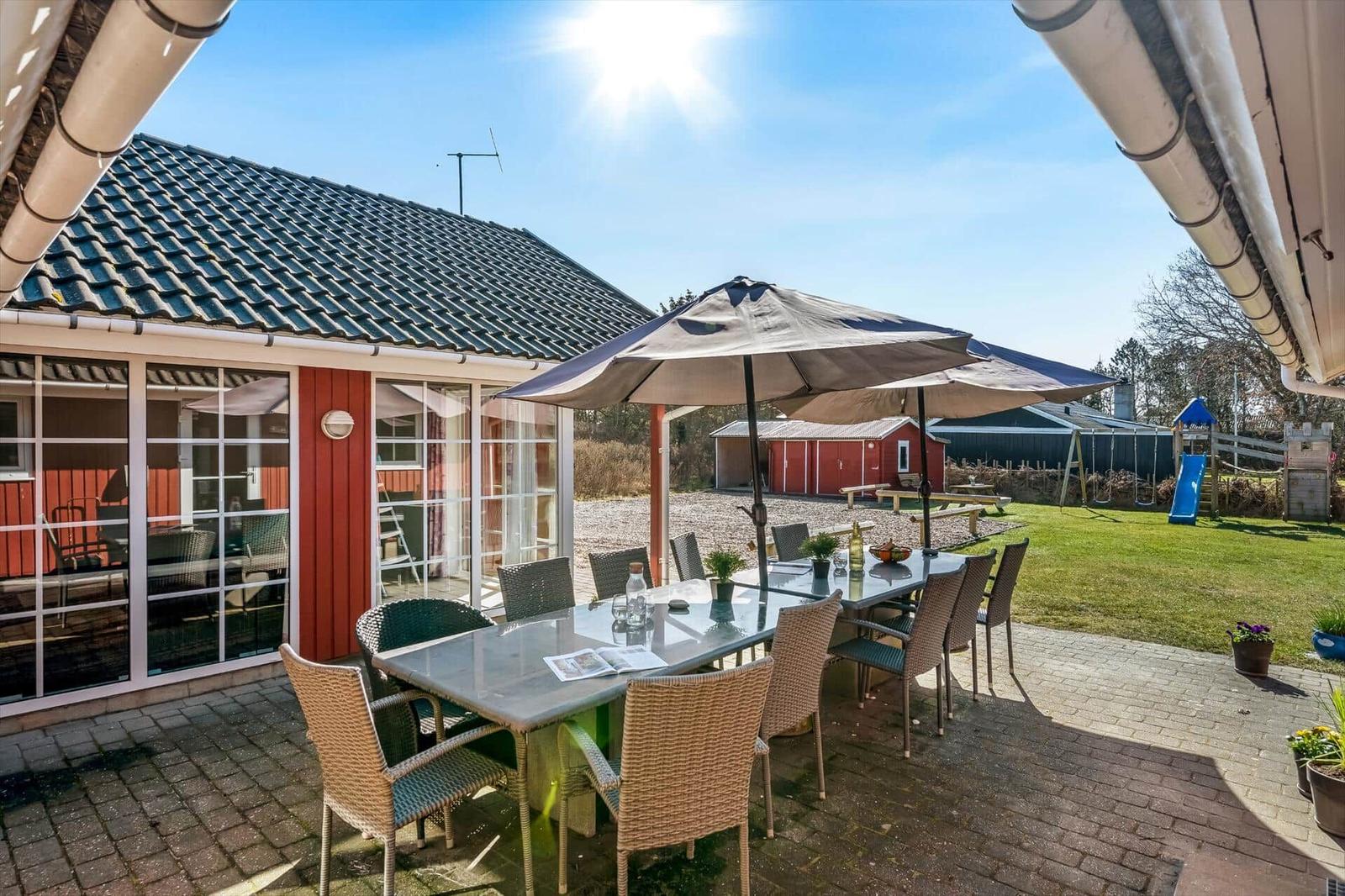 Terrace with table, chairs, and umbrella. In the background, garden and playground.
