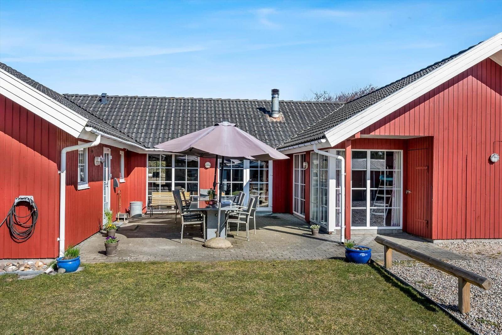 Red garden house with terrace, table, chairs, and umbrella.