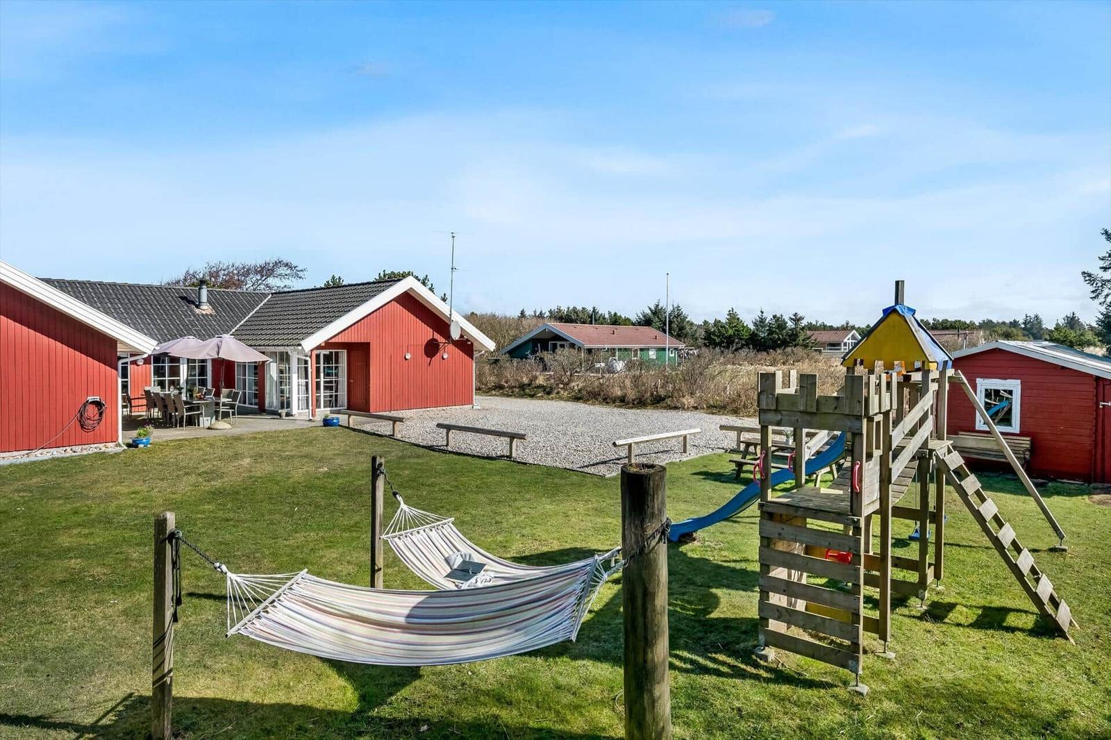 Red wooden house with garden, hammock, and playground. Outdoor table and grilling area.