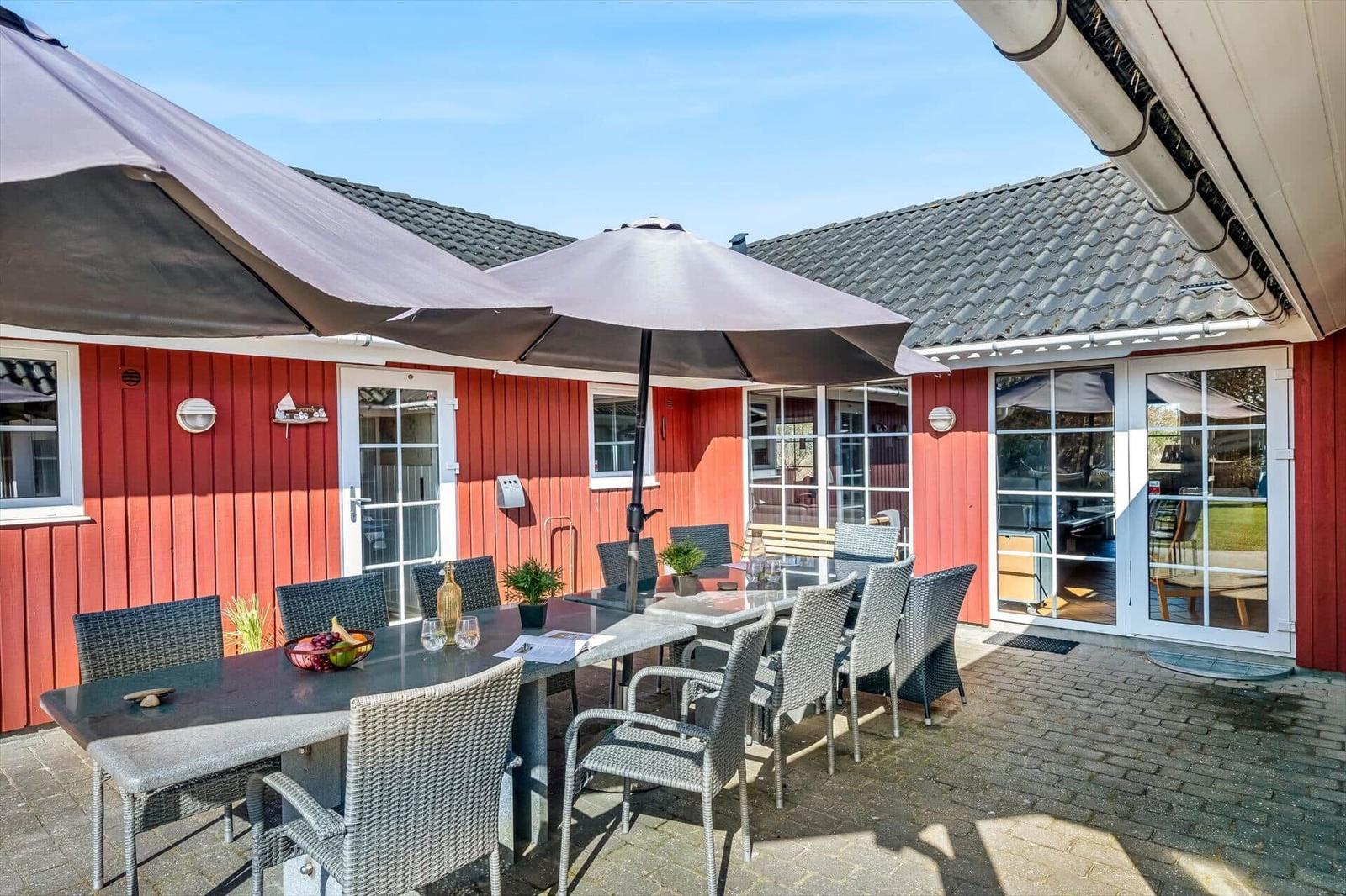 Red wooden structure with terrace, table, chairs, and umbrellas.