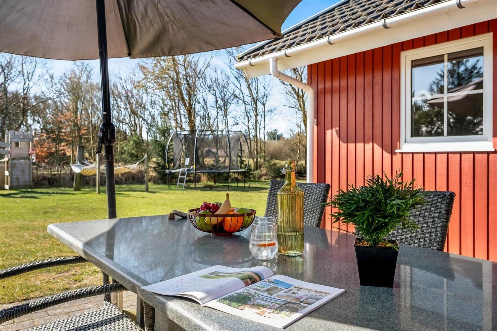 Terrace with table, chairs, and umbrella. Background: garden with trampoline and house wall.