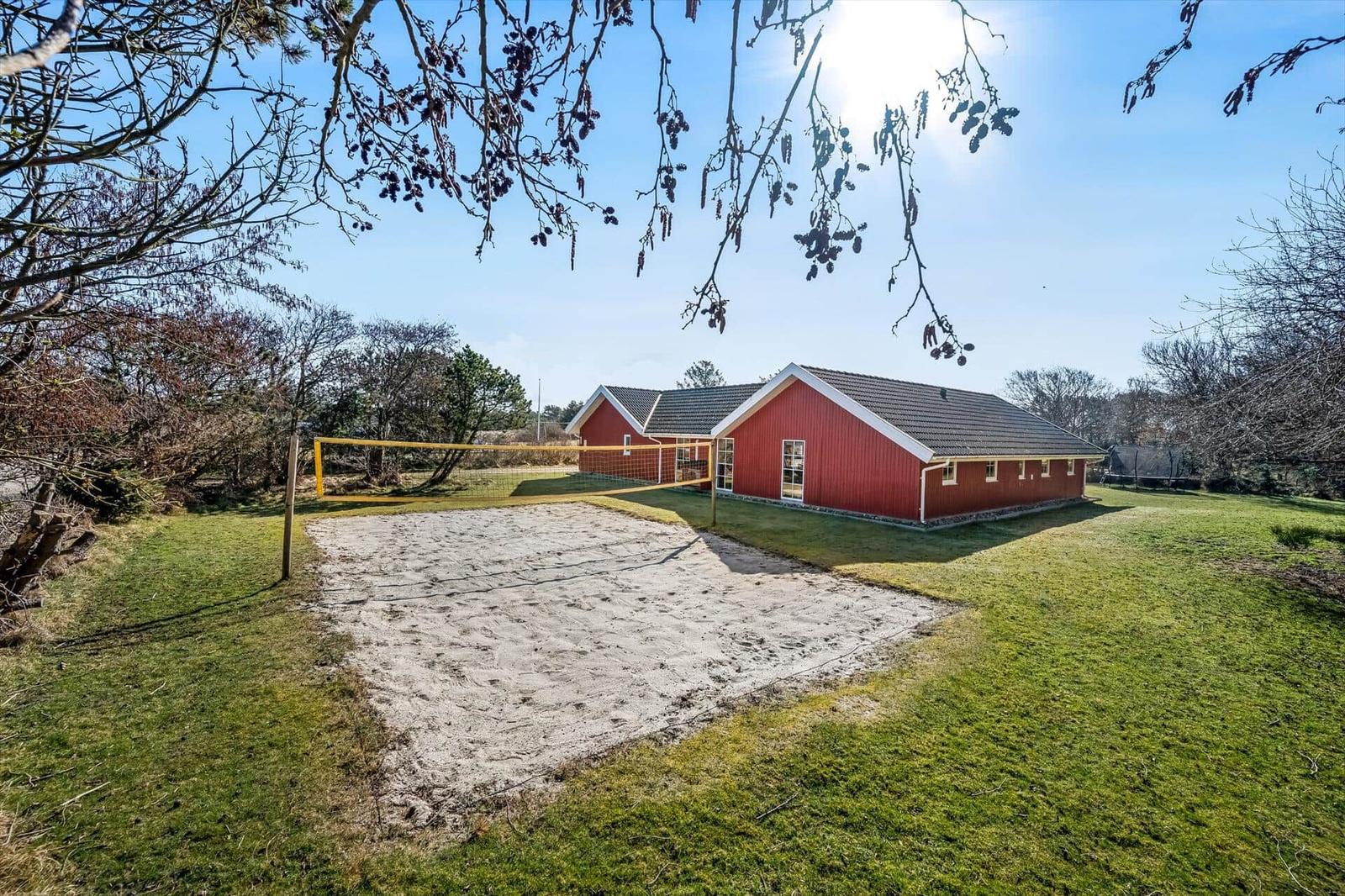 Red vacation house with sand volleyball court on green lawn.