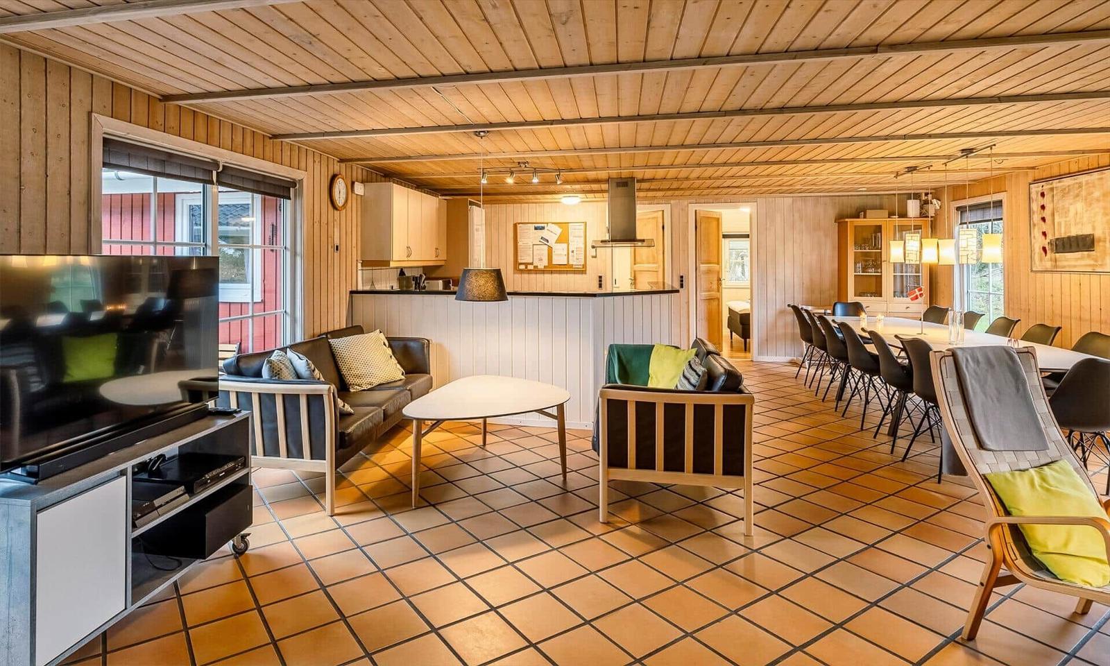 Living area with sofa, armchairs, and TV. Kitchen and dining area are visible.