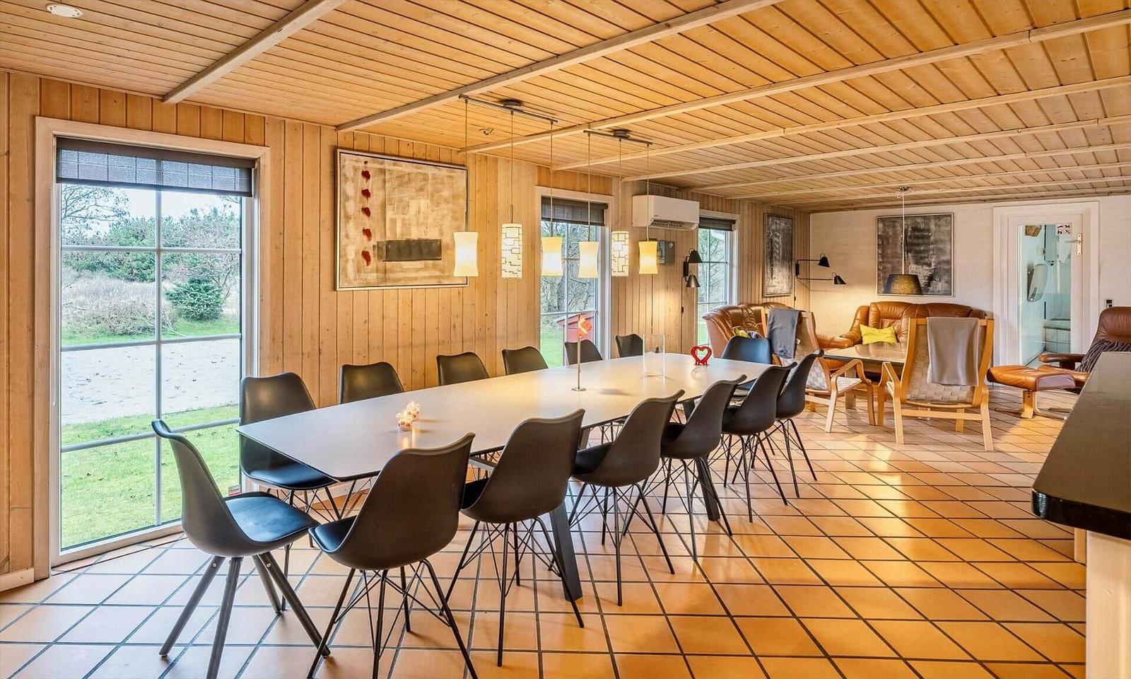 Dining area with long table and chairs, living area with leather sofas and windows.
