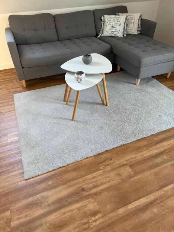 Ein grauer Ecksofa mit Kissen und zwei weißen Tischen auf Teppich.