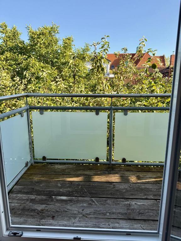 Terrasse mit Holzboden und Glasgeländer. Blick auf grüne Bäume und rote Dächer.