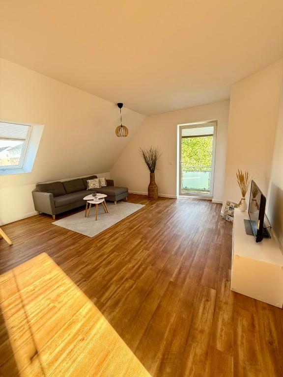 Wohnzimmer mit Sofa, TV und Balkontür. Holzboden und Dachschräge.