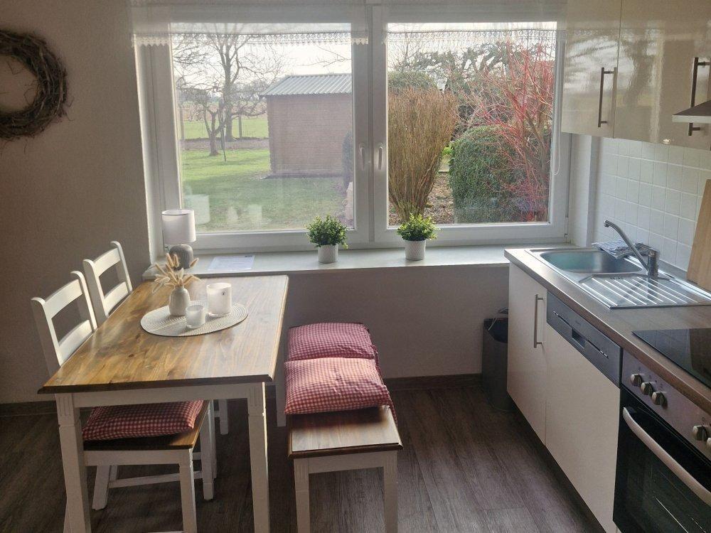 Küche mit Essbereich, Fenster mit Blick auf Garten und kleine Pflanzen auf Fensterbank.