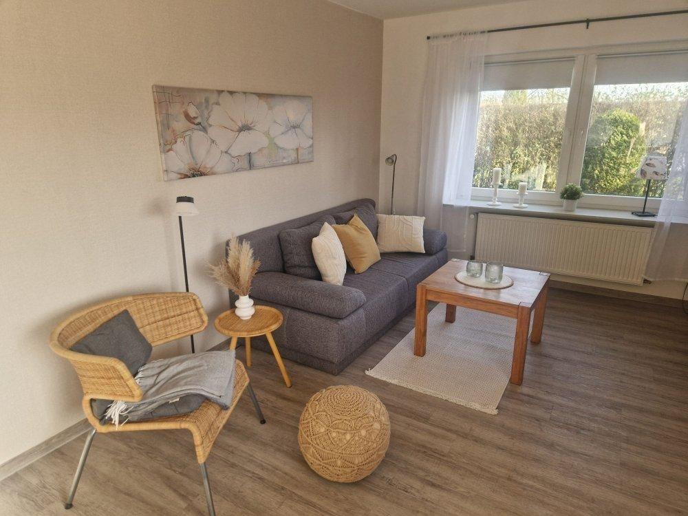 Wohnzimmer mit Sofa, Sessel und Holztisch. Fenster mit Blick auf Garten.