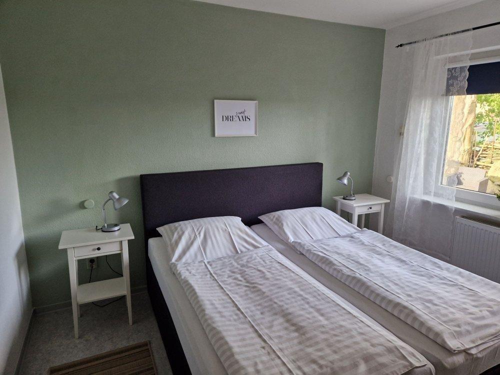 Zimmer mit Doppelbett, zwei Nachttischen und Fenster mit Blick auf Garten.