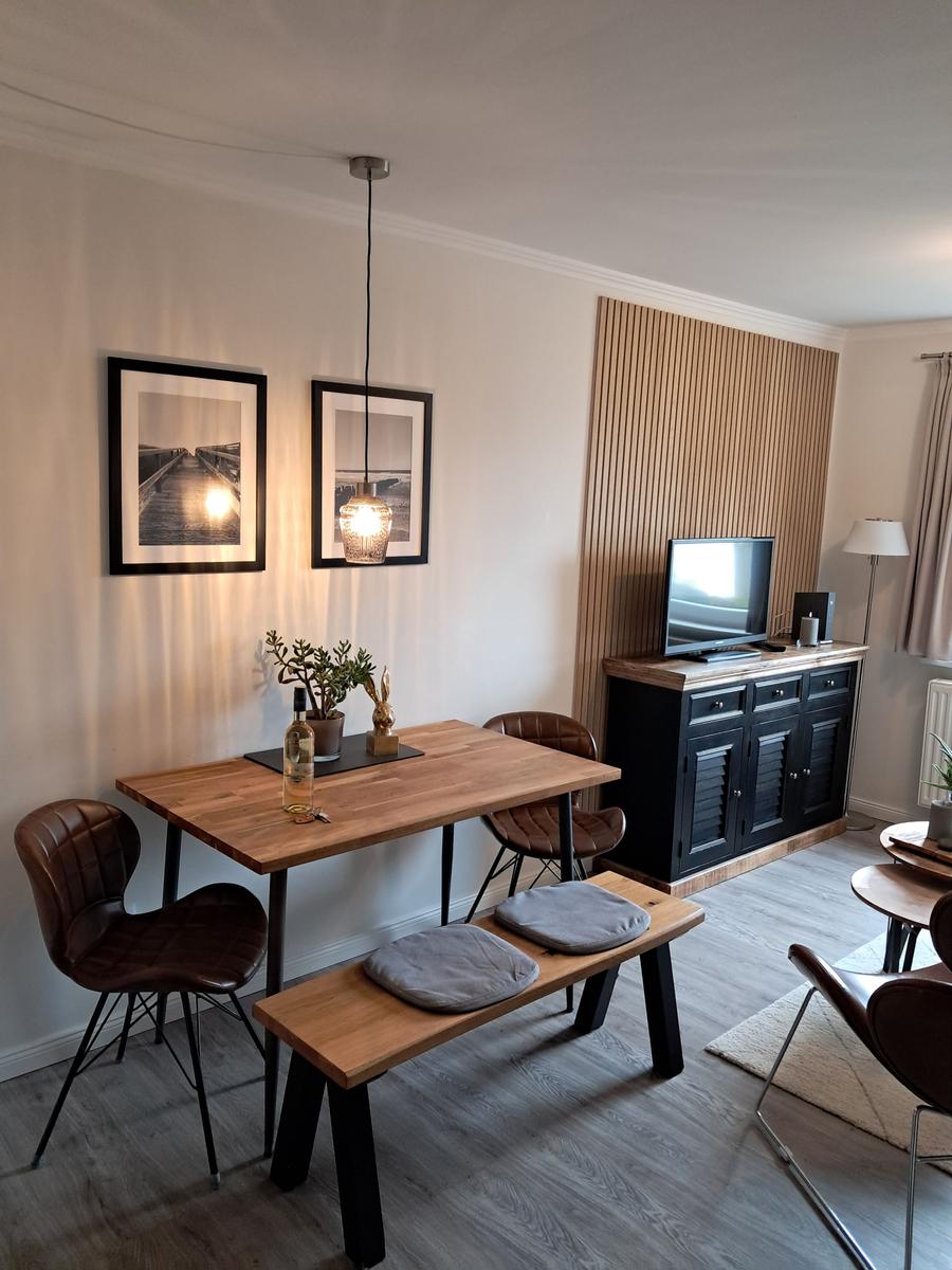 Essbereich mit Holztisch, Stühlen und TV-Schrank an der Wand.