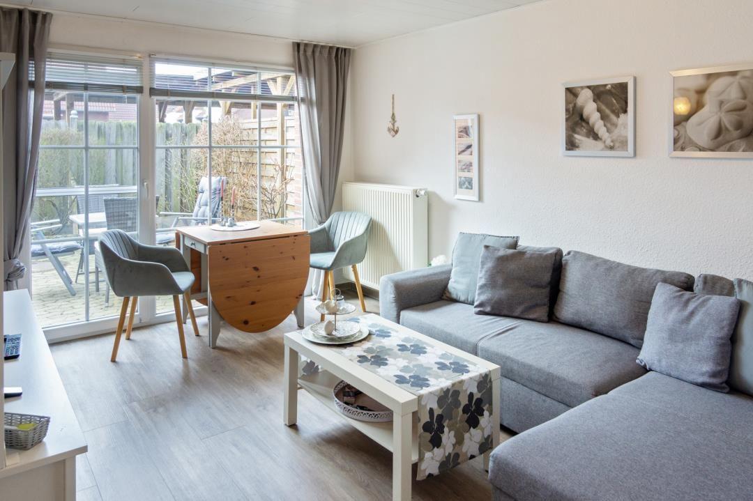Wohnzimmer mit Sofa, Tisch und Sitzgelegenheiten. Durchgang zum Garten mit Tisch und Stühlen.