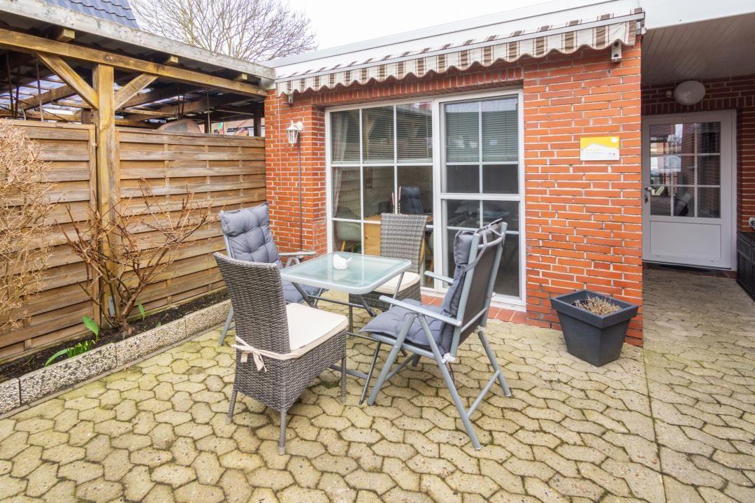 Hinterhof mit Sitzgruppe, Terrasse und Glasfront. Holzzaun und Pflanzen sichtbar.