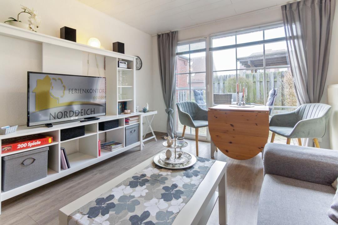 Wohnzimmer mit Fernseher, Esstisch und Sitzgelegenheiten. Durchgang zur Terrasse.