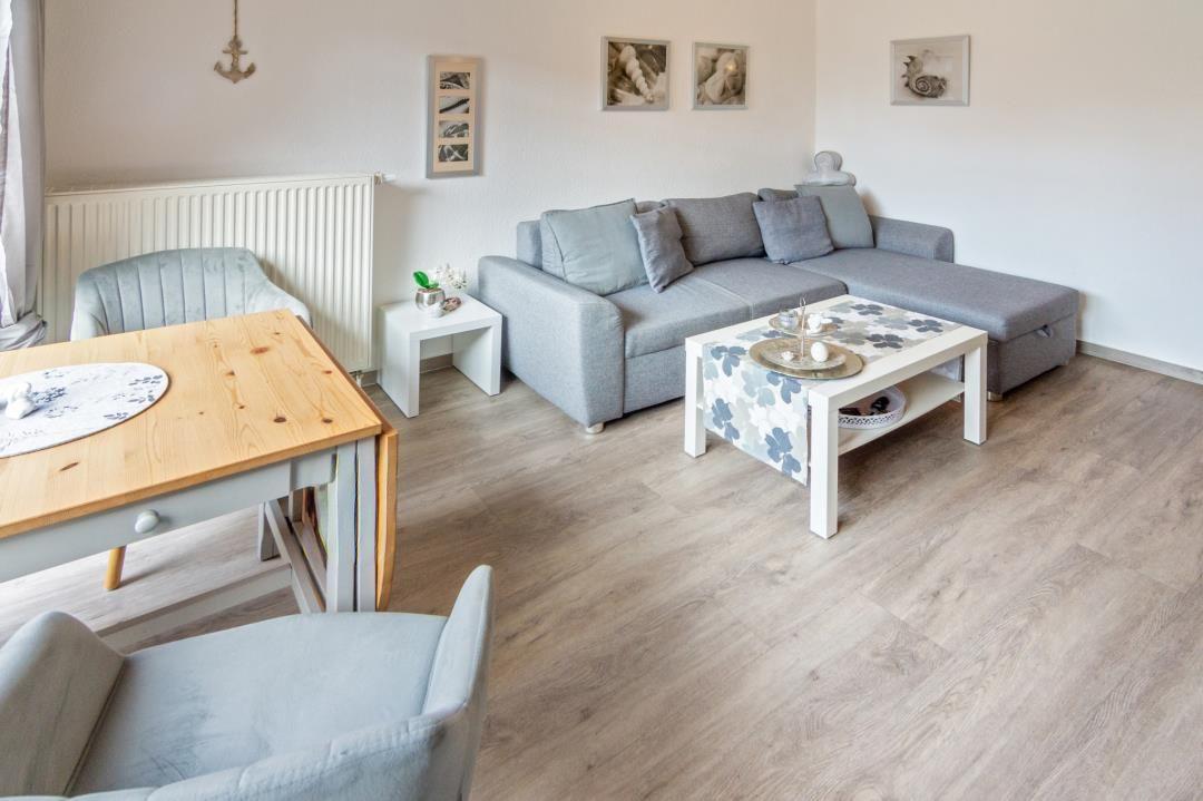 Wohn- und Essbereich mit grauem Sofa, Holztisch und hellen Wänden.