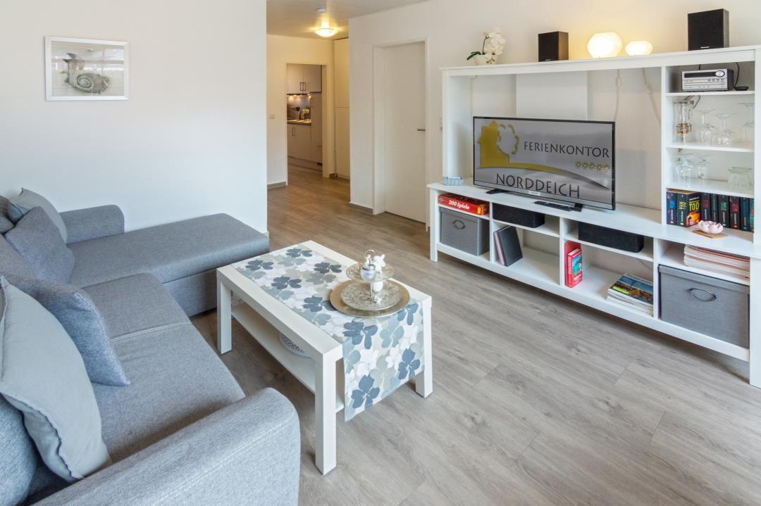 Wohnzimmer mit Sofa, Couchtisch und TV-Möbel. Küche im Hintergrund.