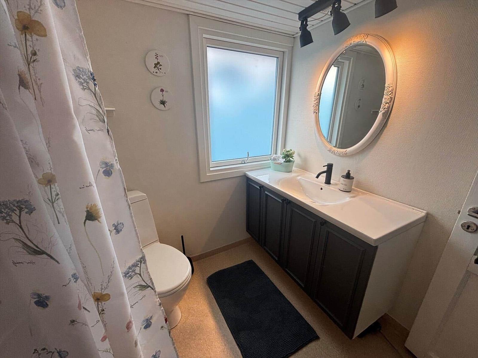 Badezimmer mit Waschbecken, Spiegel, Toilette und Dusche mit Vorhang.