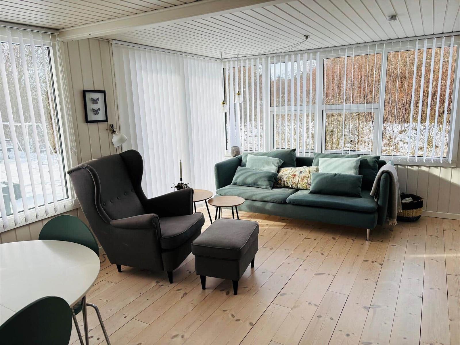 Wohnraum mit Sofa, Sessel und Holzboden. Große Fenster mit Blick auf Schnee.
