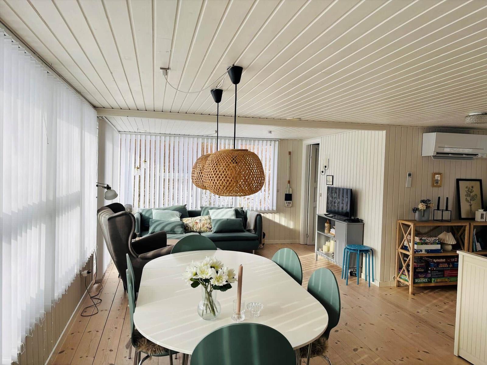 Essbereich mit runden Tisch und grünen Stühlen. Wohnbereich mit Sofa und wicker Lampe.