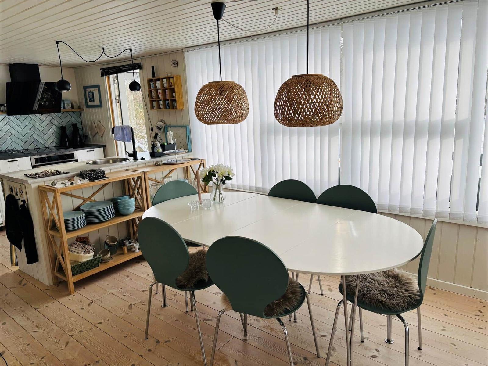 Essbereich mit ovaler Tafel und grünen Stühlen unter zwei Bambuslampen.