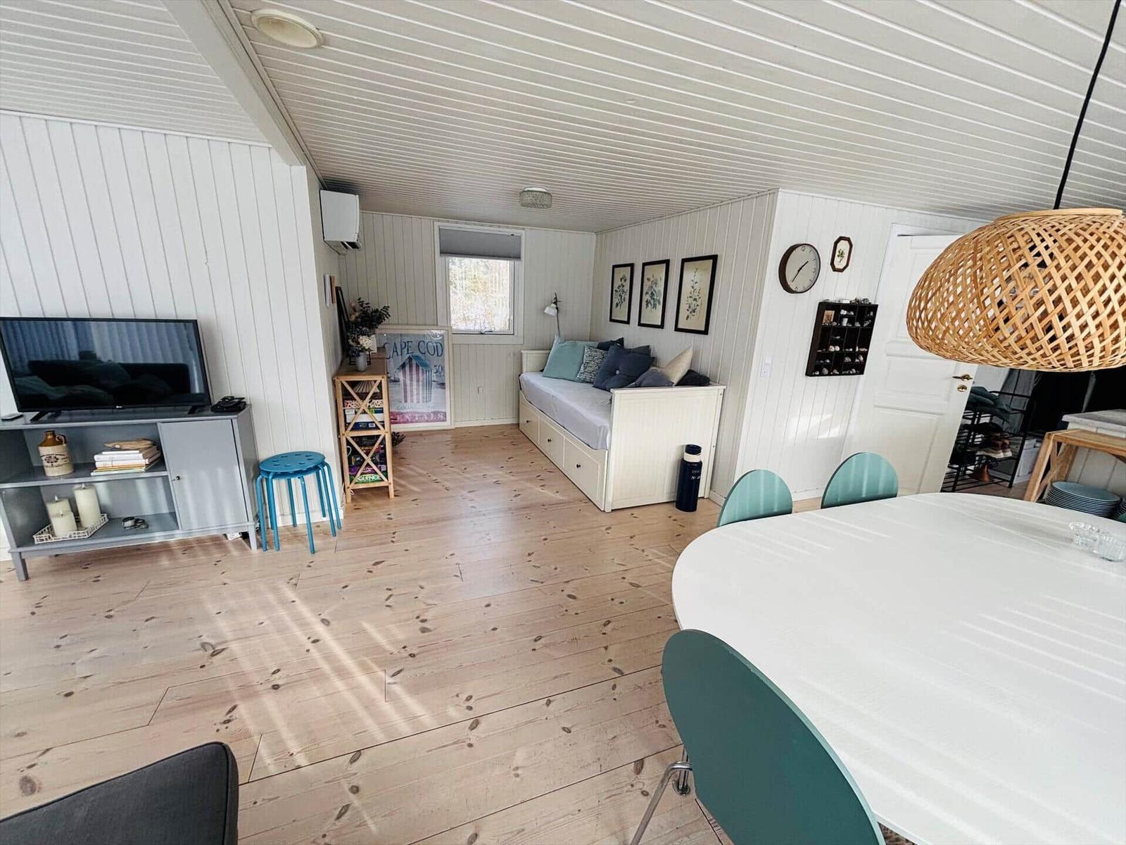 Wohn- und Essbereich mit Holzboden, Sofa, TV und Esstisch mit Stühlen.
