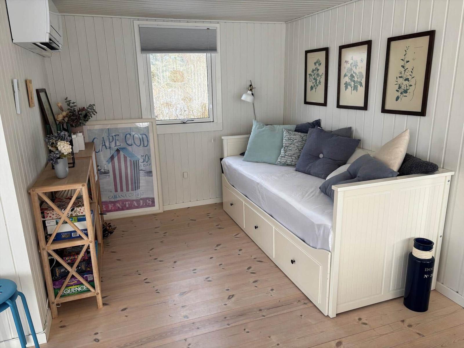 Schlafzimmer mit Bett, Fenster und Holzboden. Wanddekoration und Schrank sichtbar.