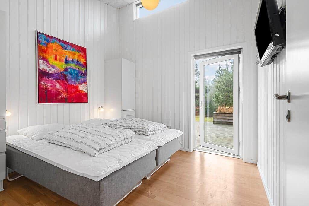 Schlafzimmer mit Doppelbett, Wandbild und Glastür zum Außenbereich.