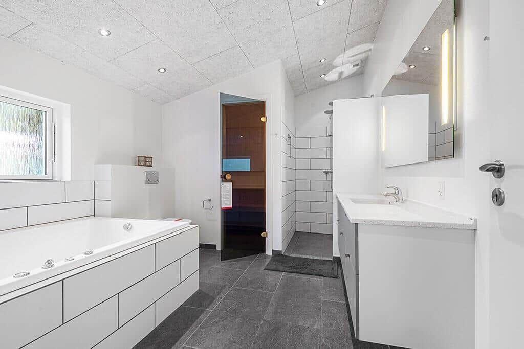 Bad mit Whirlpool, Waschbecken und Dusche. Sauna ist im Hintergrund sichtbar.