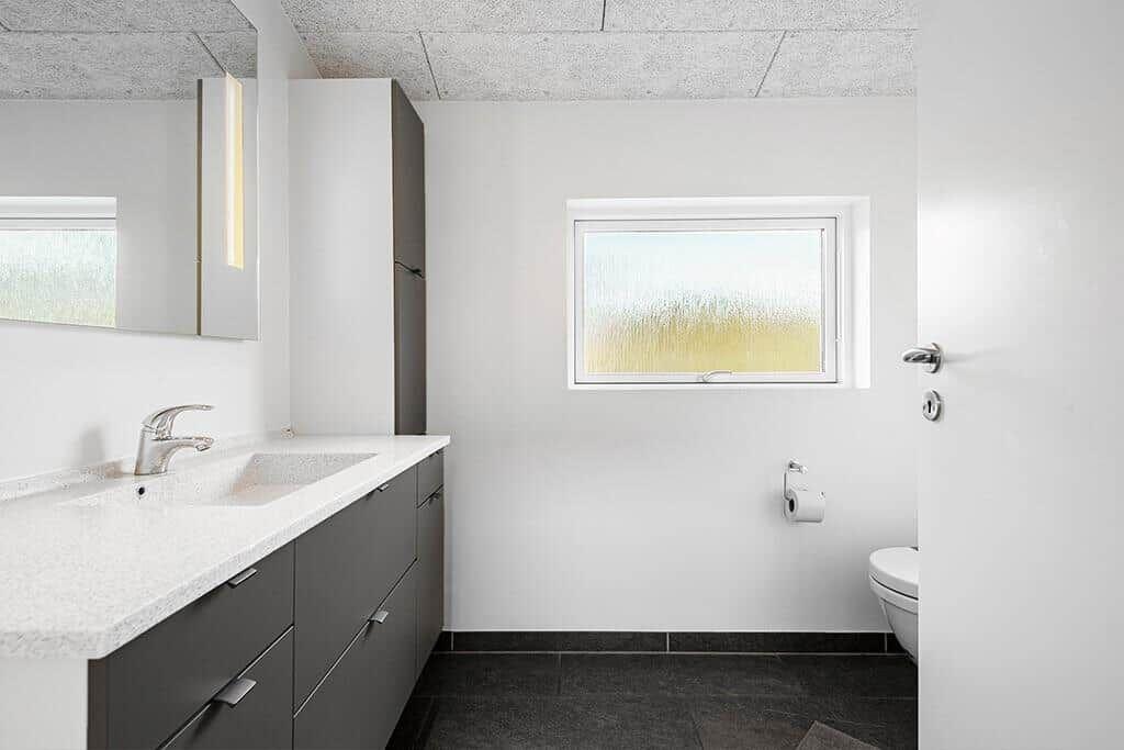 Badezimmer mit Waschbecken, Spiegel, Toilette und Fenster mit getöntem Glas.