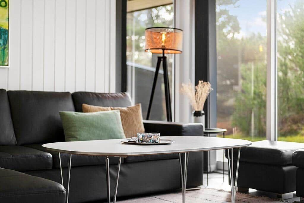 Ein Wohnzimmer mit schwarzer Couch, runder Tisch und großem Fenster.