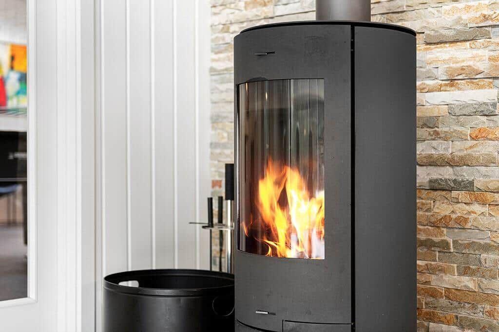 Schwarzer Kaminofen mit brennendem Feuer an Steinwand