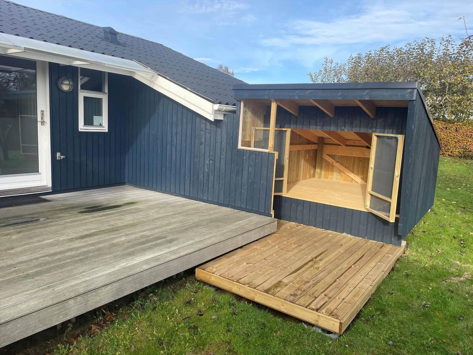 Ein Holzveranda mit offener Garage und Terrasse an einem Haus mit dunkelblauer Fassade.