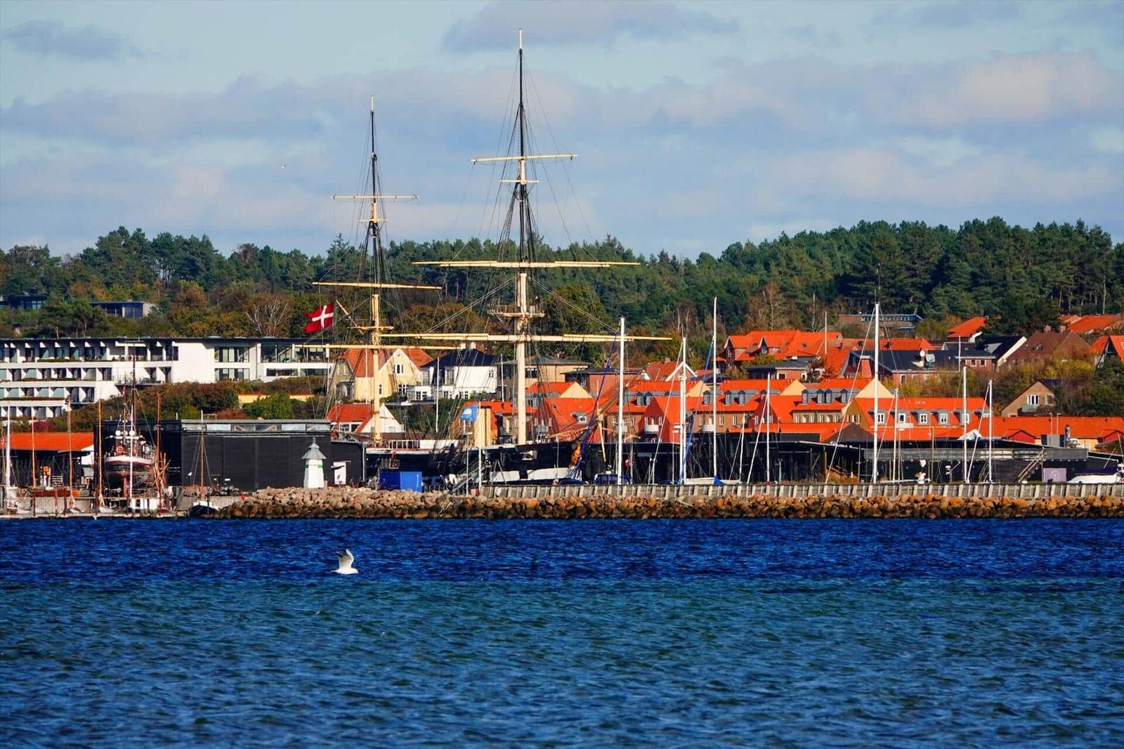 Hafenstadt mit Segelschiff und roten Dächern am Wasser