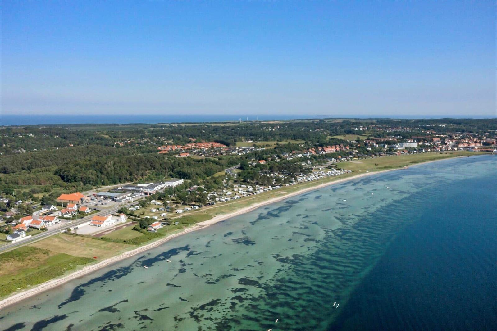Aerial view of coastal area with beach, campsite, and residential buildings near the sea.