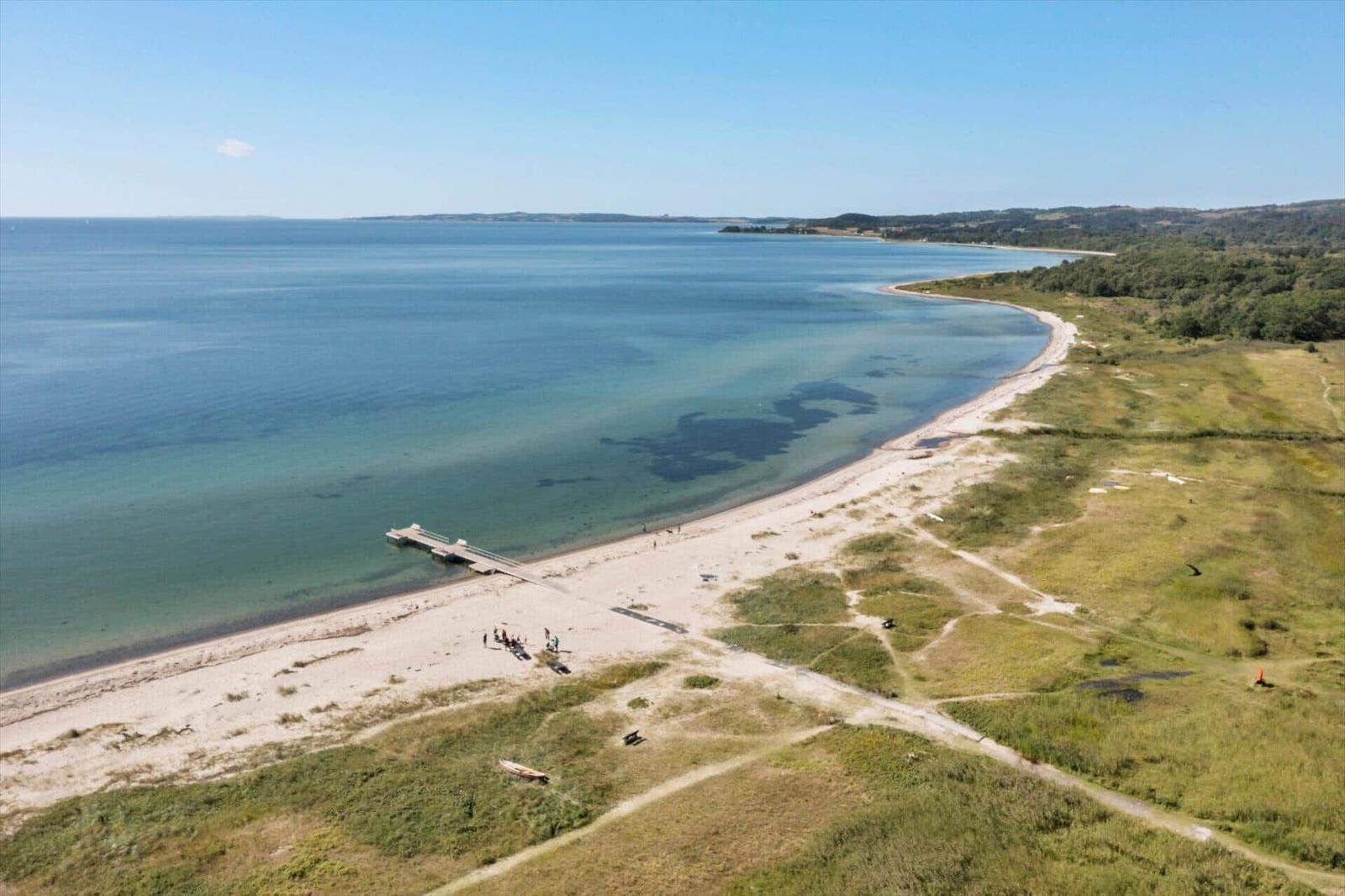 Strand mit Steg und grüner Landschaft entlang des Wassers.