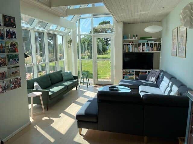 Wohnbereich mit Sofa, Fernseher und großem Fenster zur Gartenansicht.